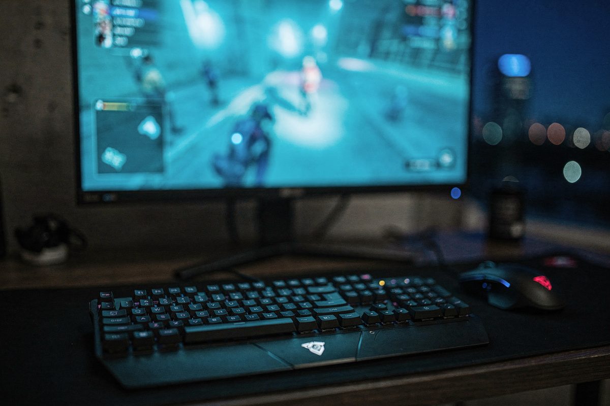 A gaming battlestation at night with a mechanical keyboard and mouse lit by a glowing monitor